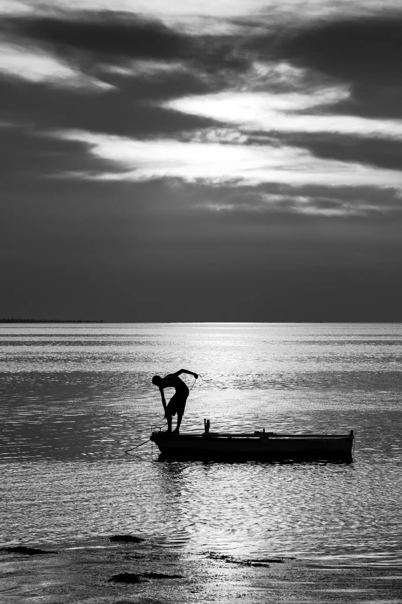 Silhouette sur une petite embarcation sous un ciel nuageux