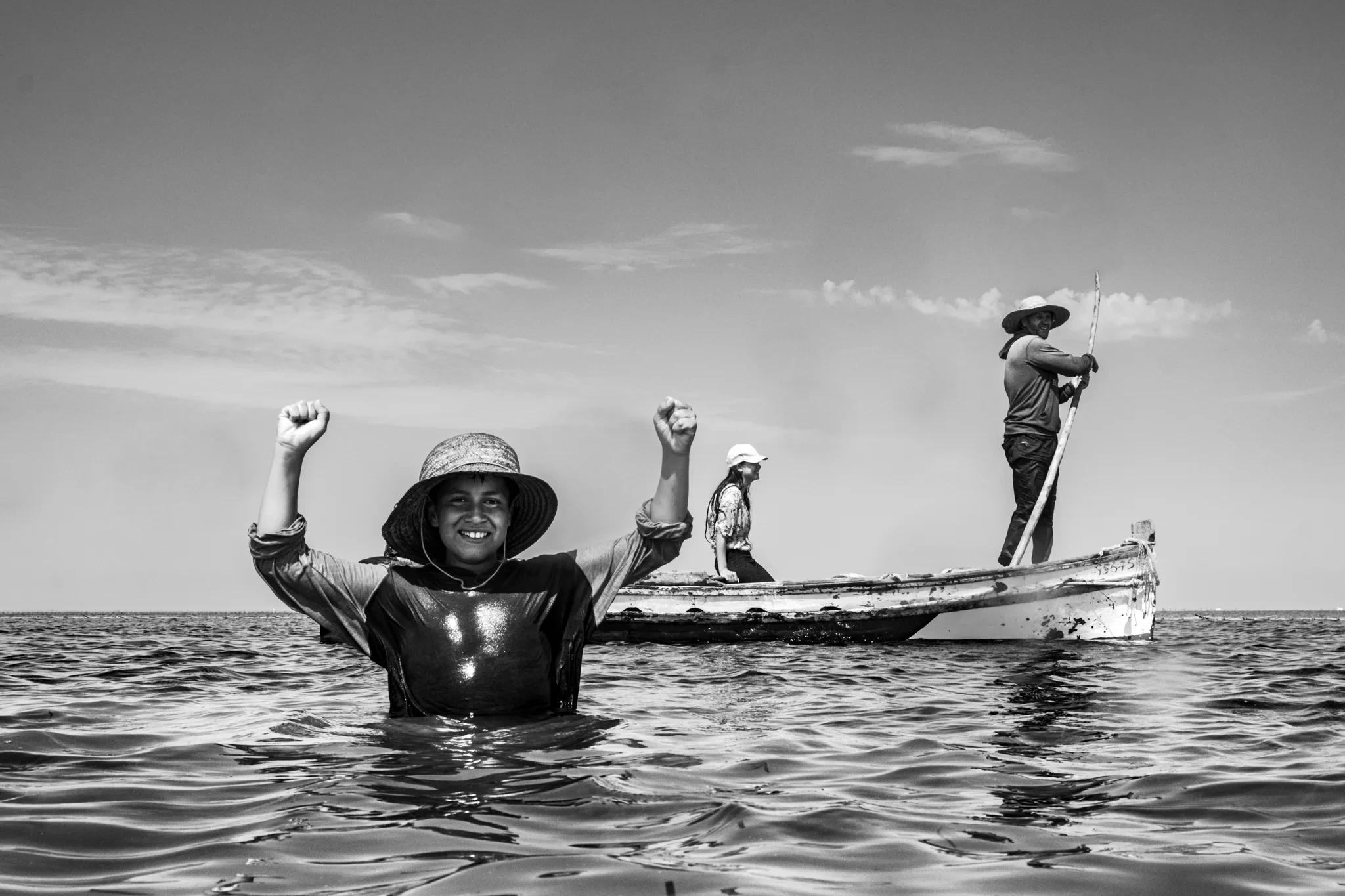 Un baigneur souriant lève les bras devant un bateau
