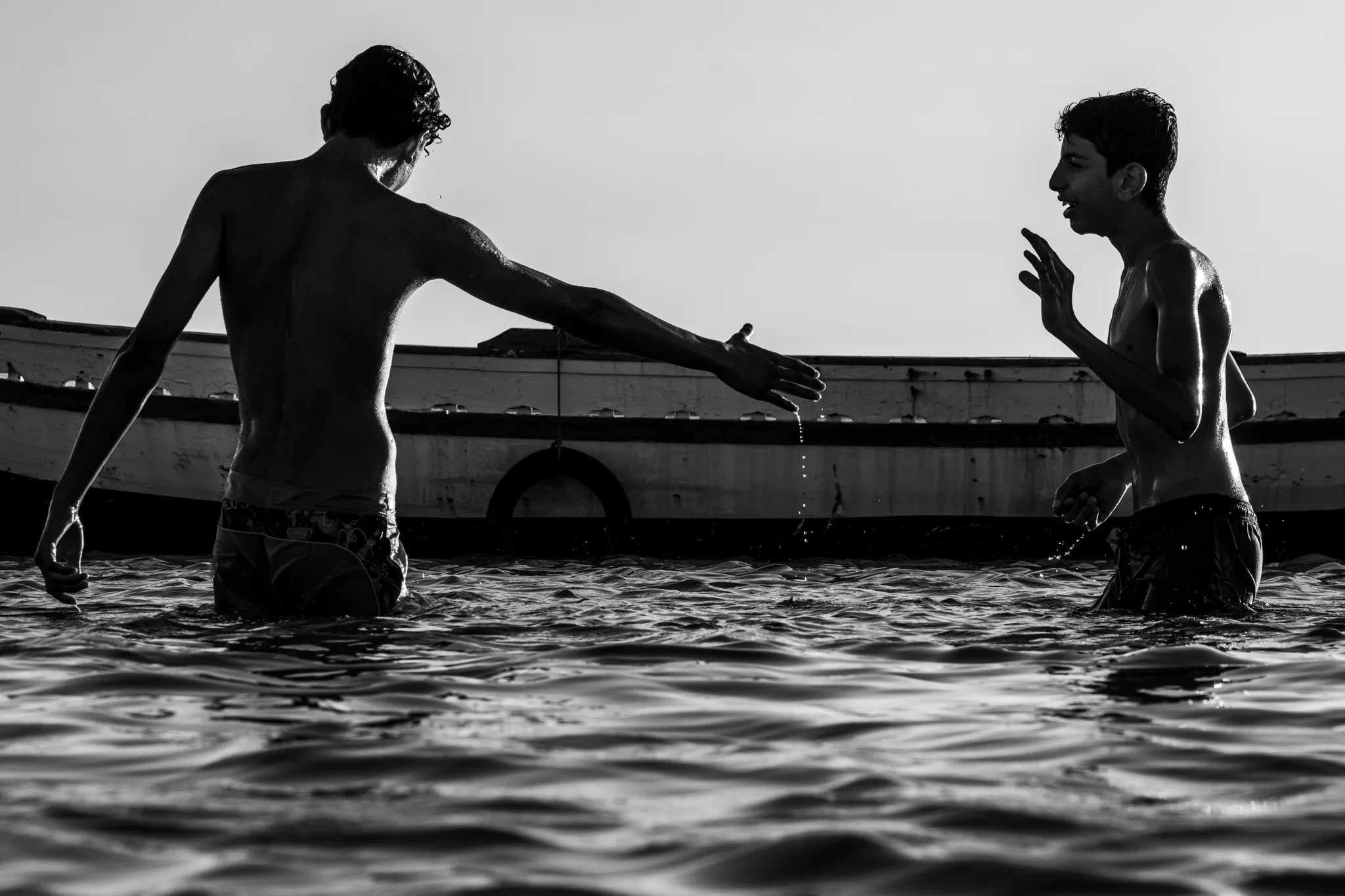 Deux jeunes se font face dans l’eau devant un bateau