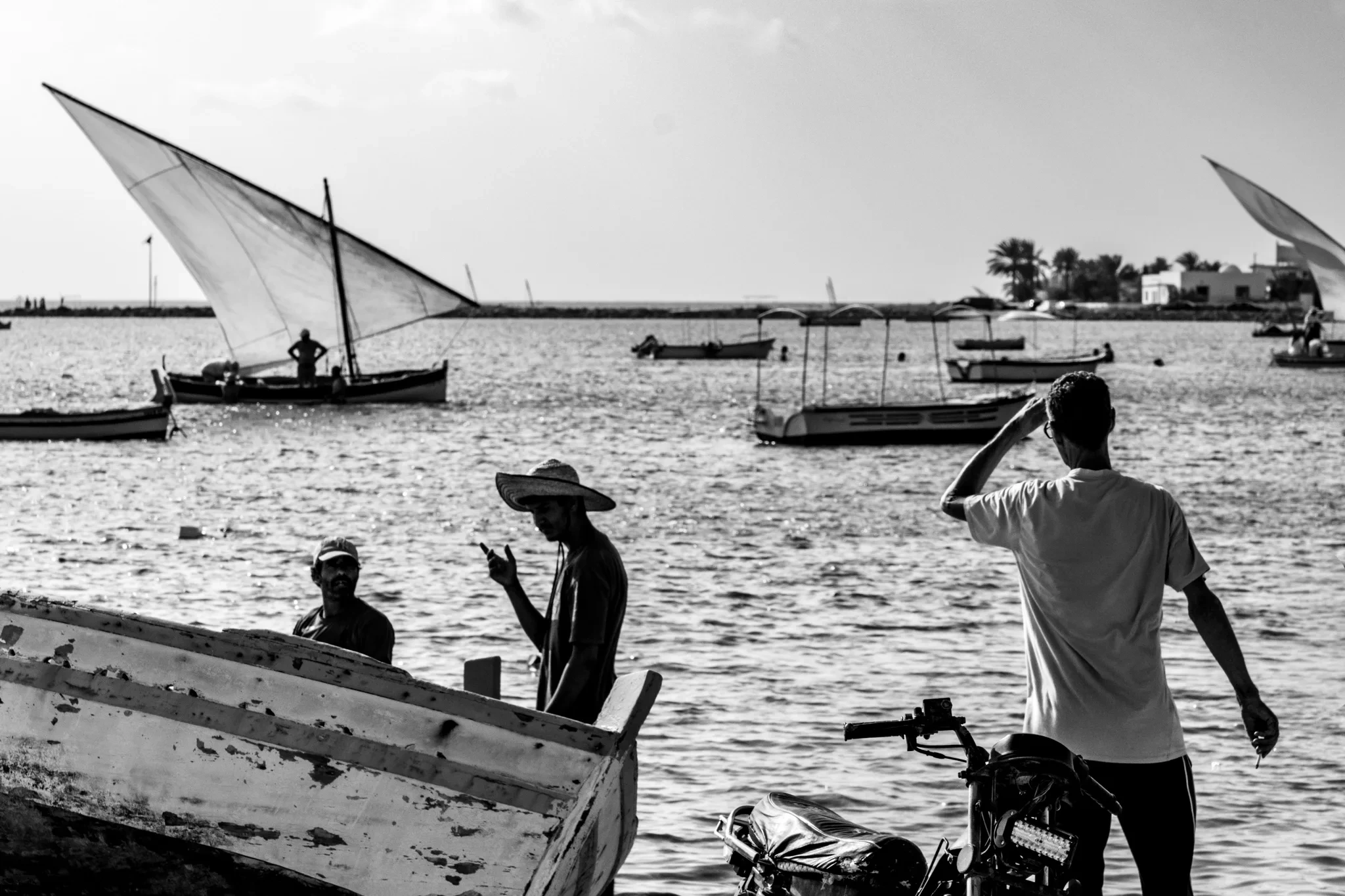 Bateaux, baigneurs et voile latine près du rivage