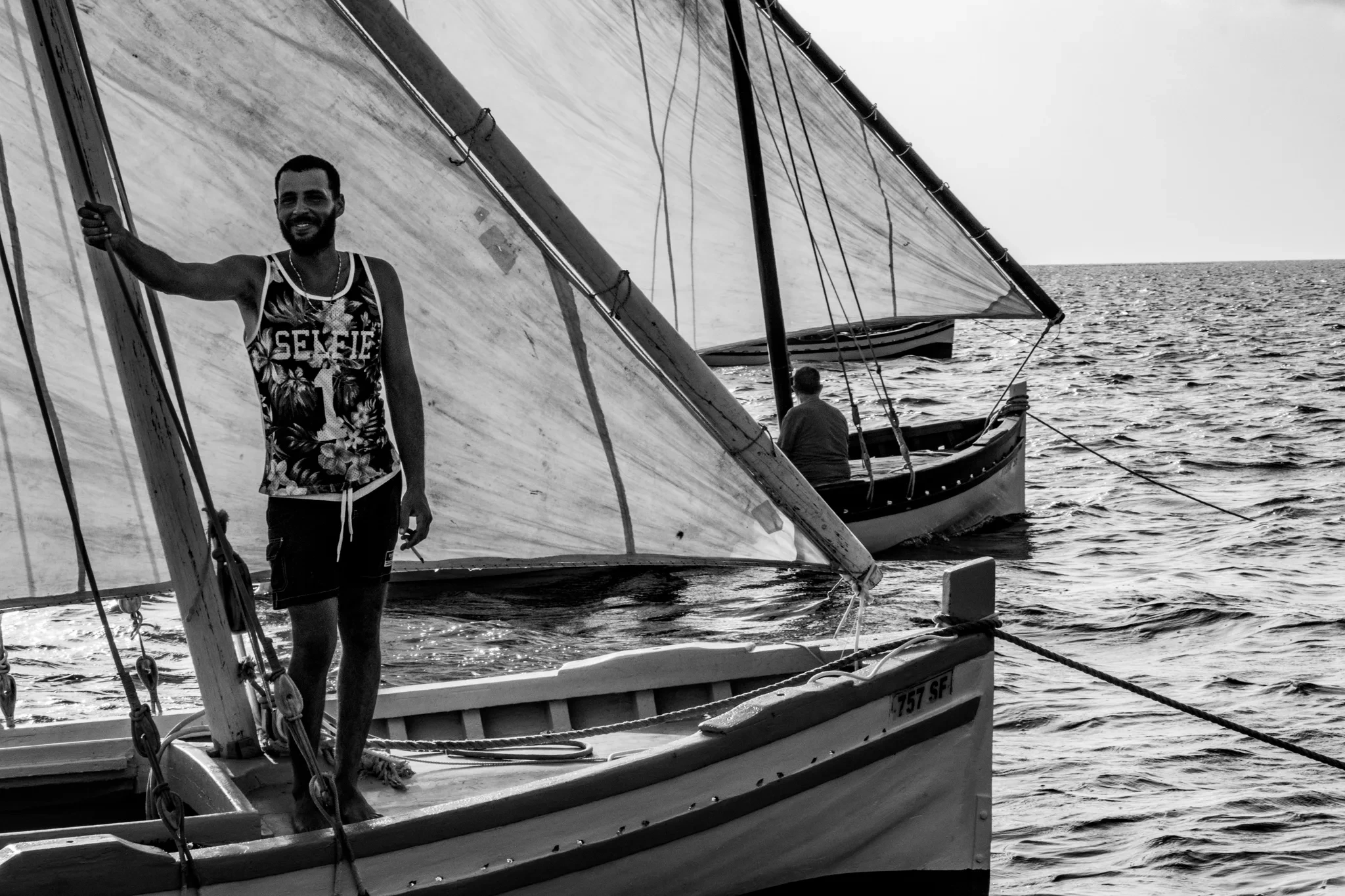 Jeune debout dans un bateau, voile déployée derrière lui