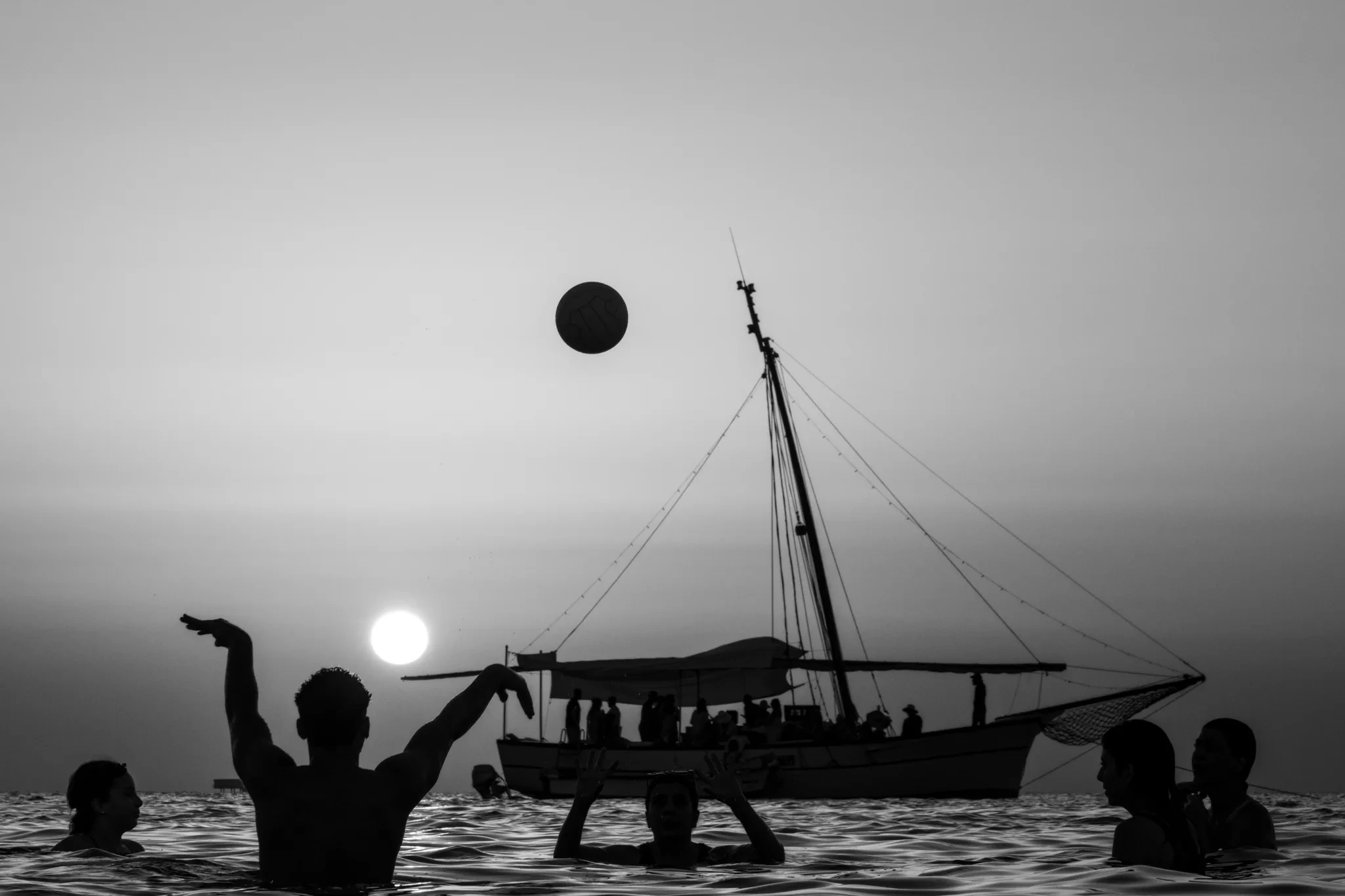 Jeu de ballon dans l’eau devant un bateau au coucher du soleil
